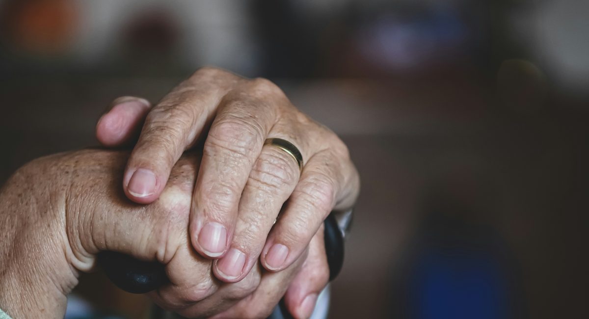 Elderly hands on a walking cane — the caregiving moment